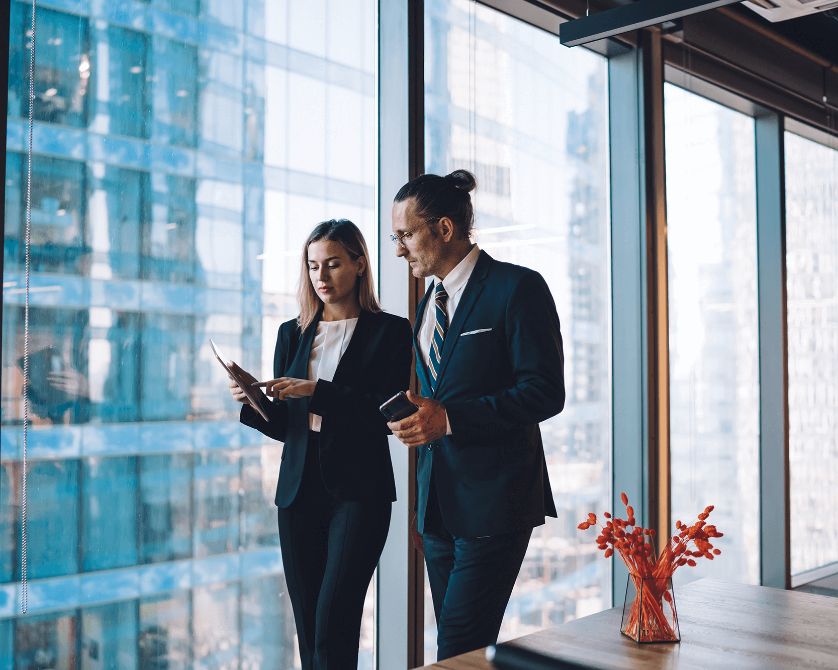 Zwei Geschäftsleute stehen vor einer Fensterfront und besprechen Unterlagen auf einem Tablet.